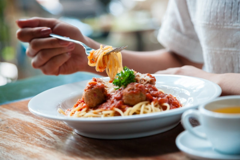 It's easier to get true nourishment from your food when you have a peaceful relationship with food. Photo of a woman's hand as she scoops some pasta from a shallow white bowl of spaghetti and meatballs.