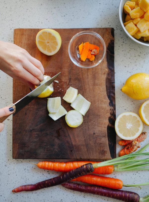hands cutting lemon on a wooden board with mango and carrots