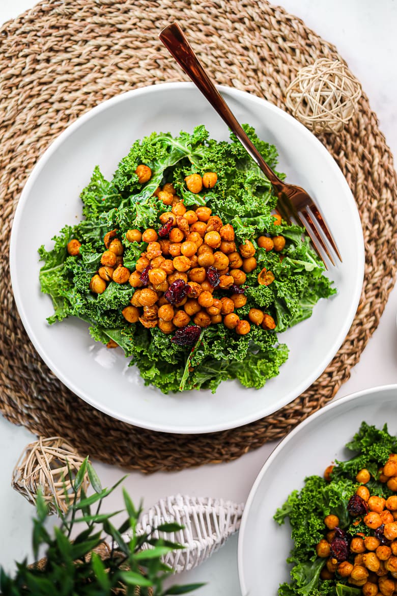 flatlay shot of two bowls of kale salad with spicy roasted chickpeas and dried cranberries ontop.