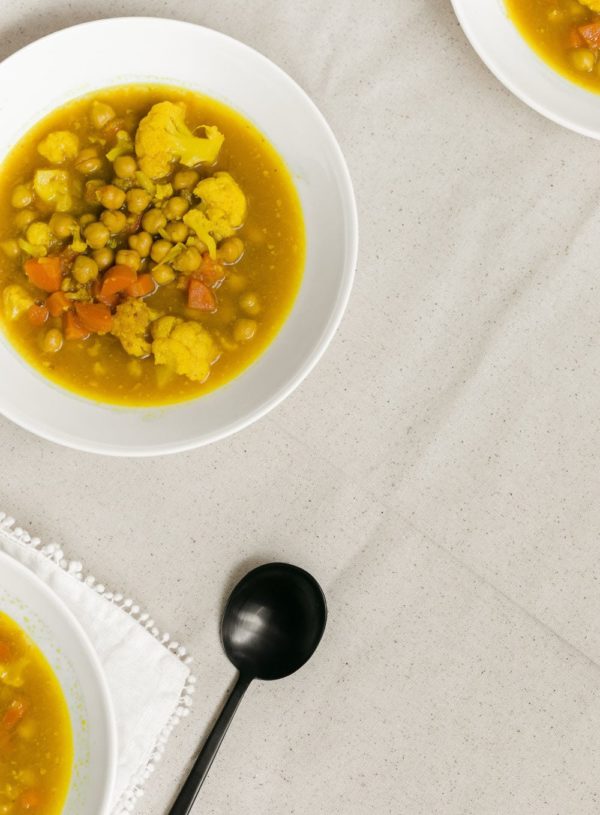 turmeric ginger soup with cauliflower in white bowl beside a black spoon