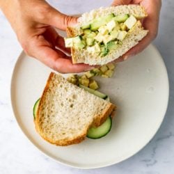 hands holding vegan egg salad sandwich on white plate