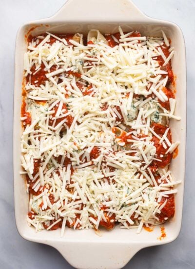 stuffed shells, sauce, and cheese in baking dish before baking.
