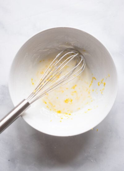 lemon loaf glaze in white bowl with whisk.