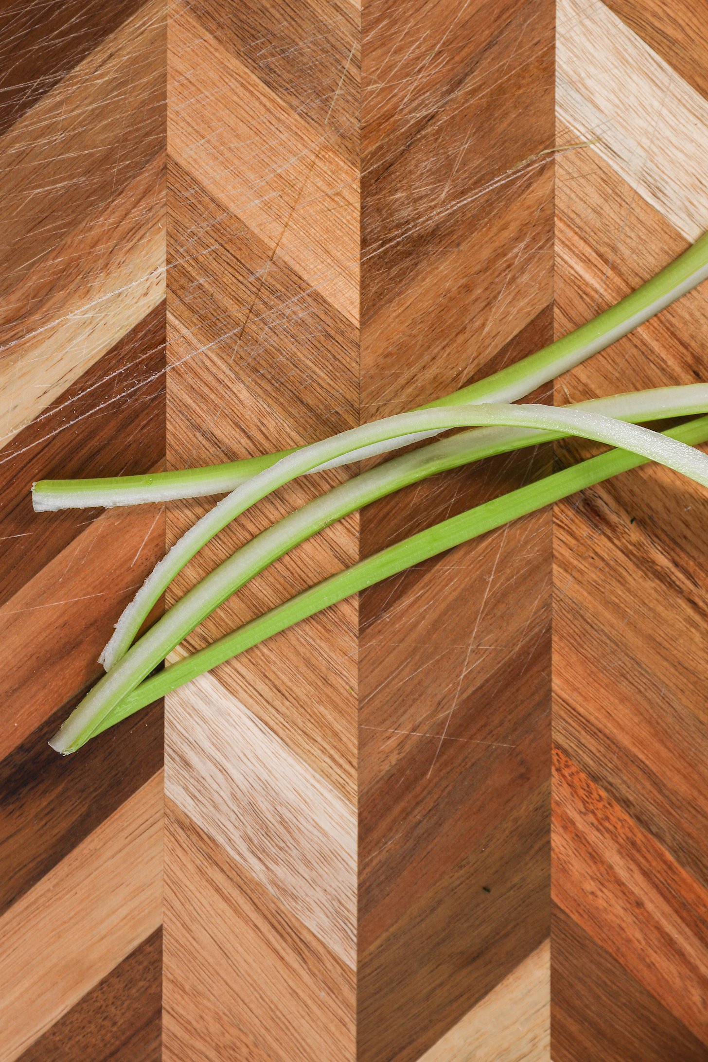 Four strips of celery piled on top of one another on a checkered wooden board.