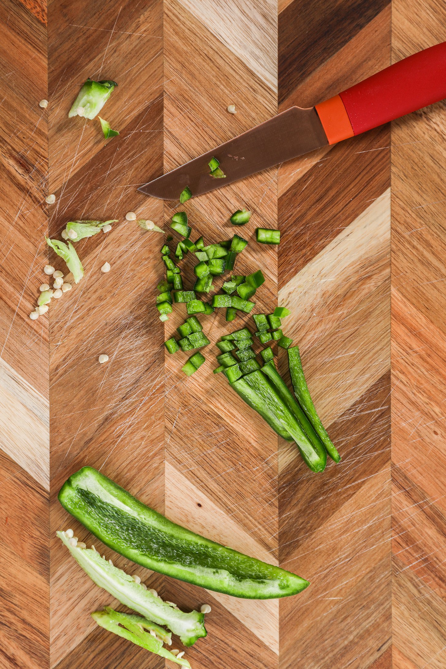 Finely chopped and strips of green chilli pepper on a checkered wooden board with a red knife.