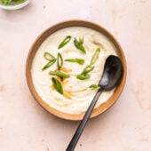 creamy parsnip soup in brown bowl with green onions and spoon