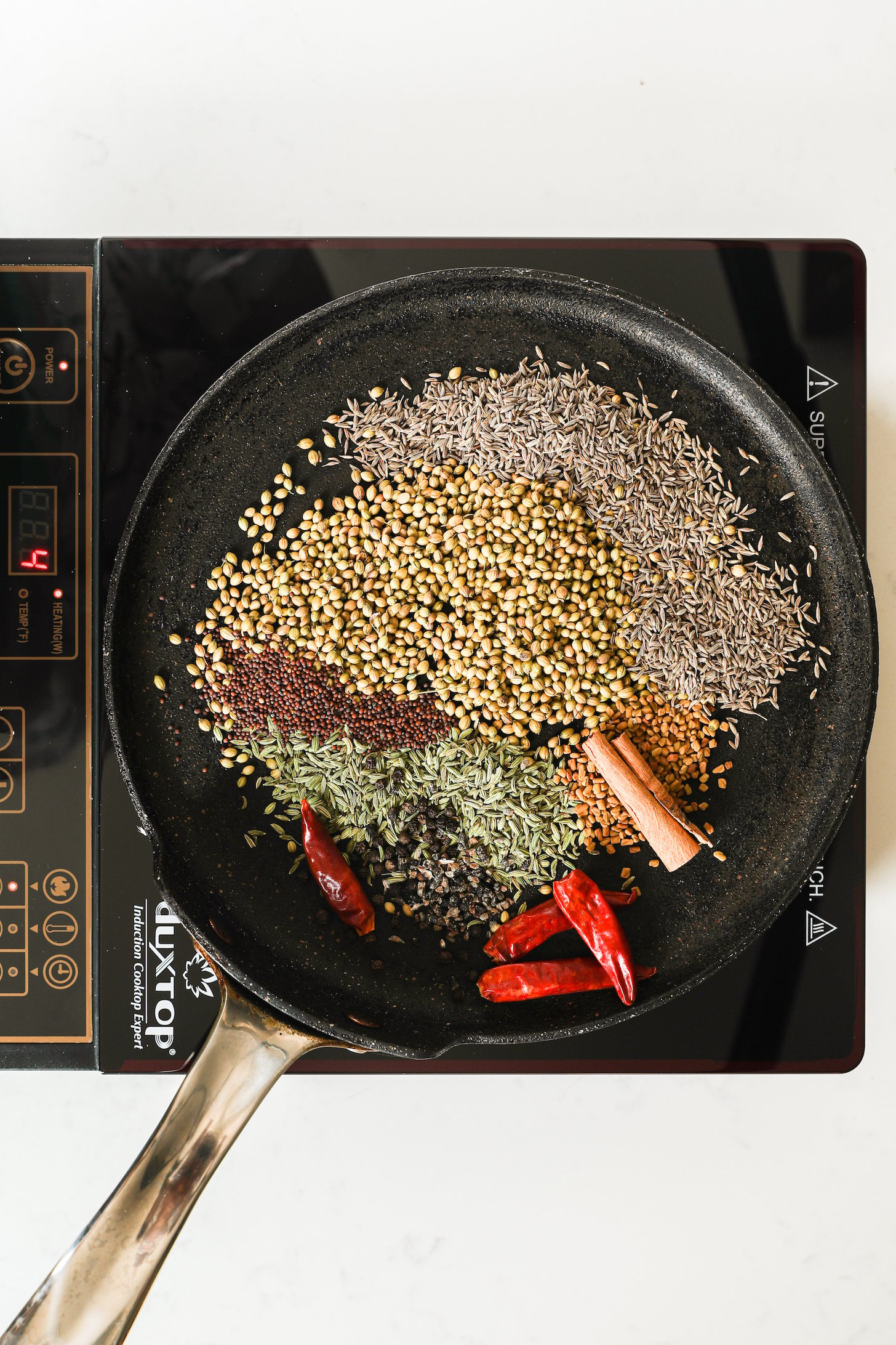 A traditional Indian girdle (tava) with South Asian whole spices on a mobile cooktop.