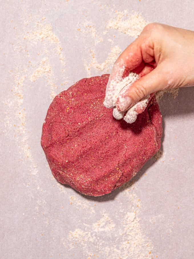 hand adding flour to pink cookie dough