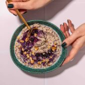 hand holding blue bowl of quinoa porridge with blueberries
