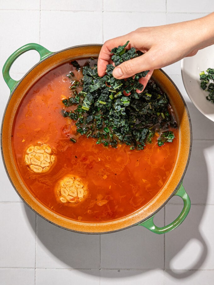 hand adding kale to pot with garlic