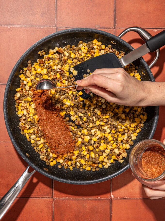 hand pouring taco seasoning on lentils and walnuts in skillet